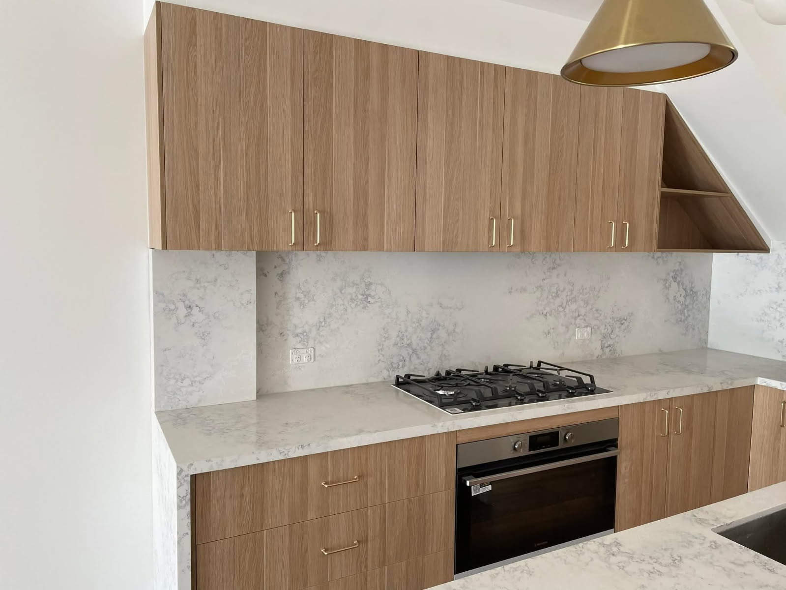 Timber veneer kitchen cabinets with stone benchtop and brass handles